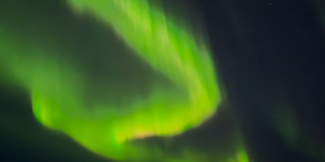 Aurora borealis berwarna hijau tampak menghiasi langit malam di atas perairan, menciptakan pemandangan memukau. (Foto: Threads/@alex_smile1313)
